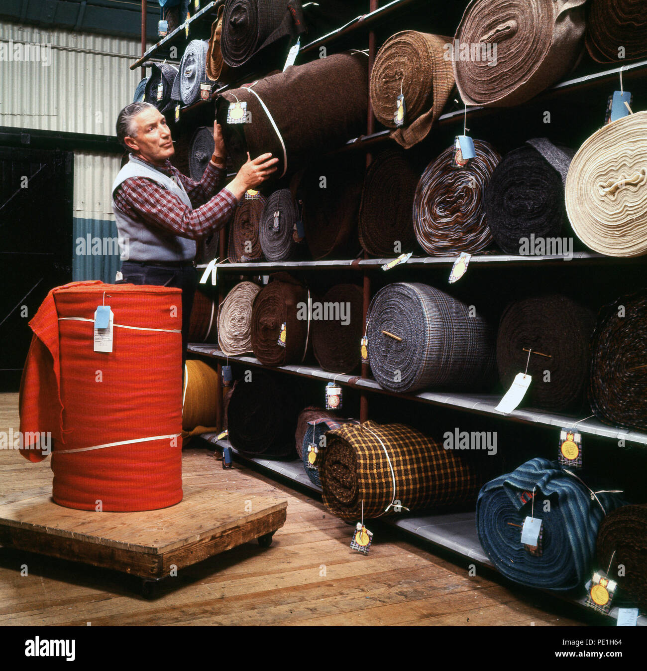 Anni sessanta, lavoratore di sesso maschile la rimozione di un rotolo finito di Harris Tweed da un ripiano in un magazzino, Highlands scozzesi, Scotland, Regno Unito. Foto Stock