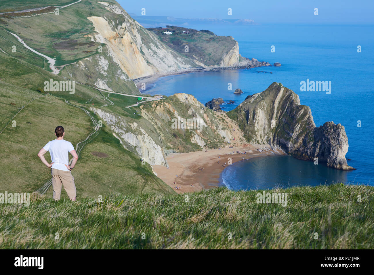 Uomo di mezza età con le mani sui suoi fianchi, guardando verso il basso in corrispondenza di una vista costiera di Durdle porta sul Jurassic Coast nel Sud Inghilterra Foto Stock