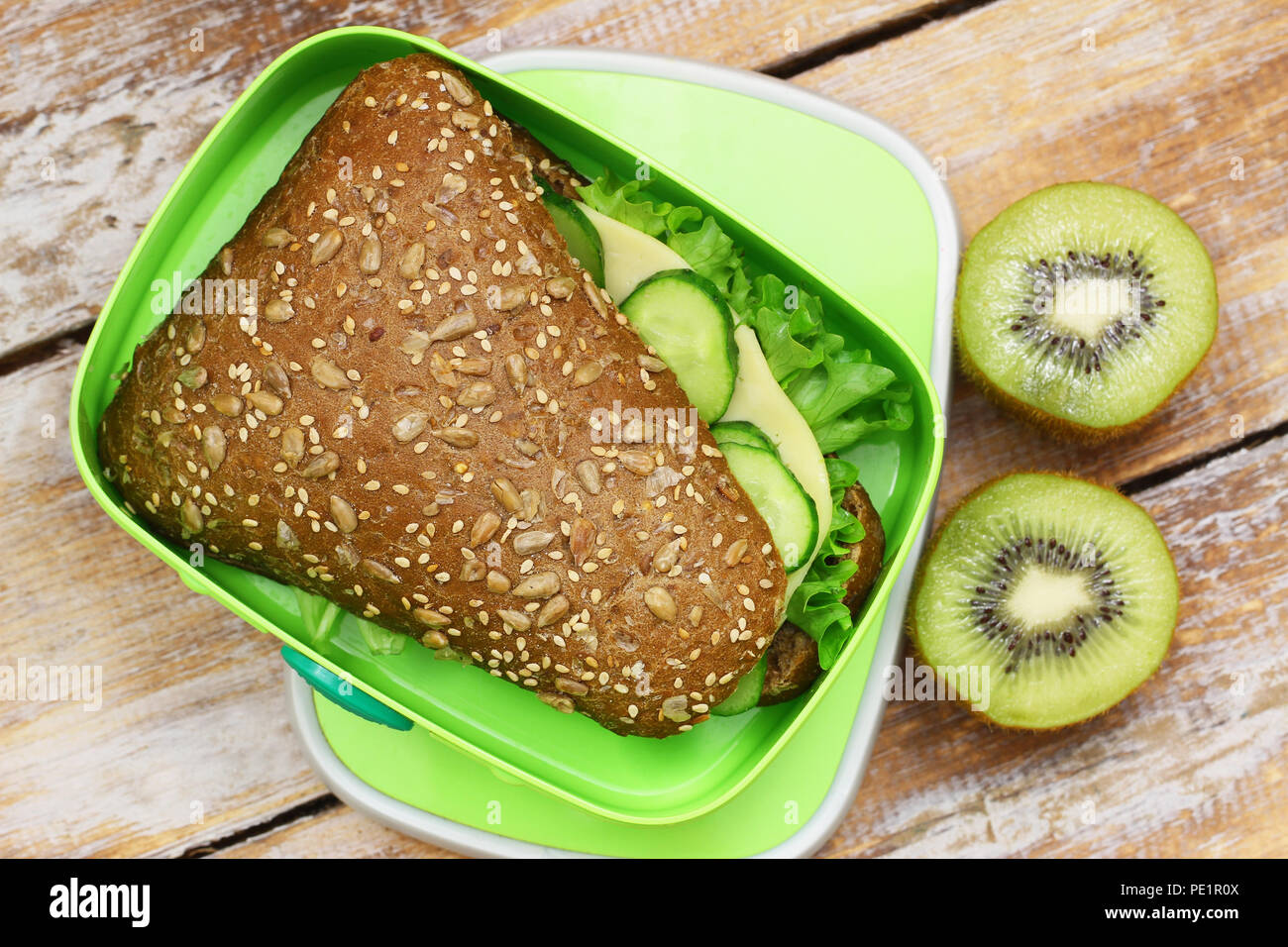 Scuola di sano pranzo scatola contenente marrone rotolo di formaggio e kiwi Foto Stock