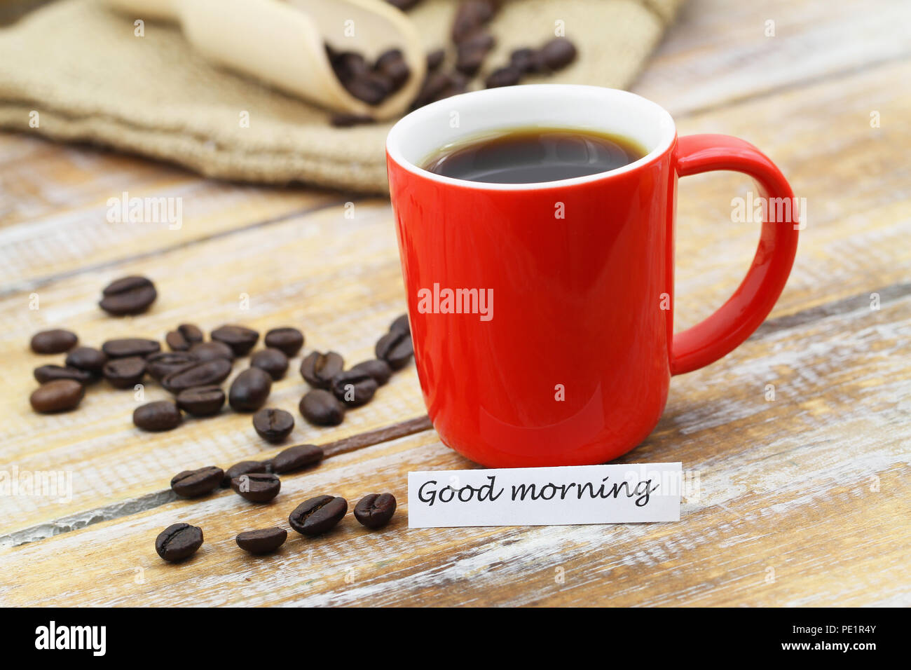 Buona mattina con carta red tazza di caffè, sparse per i chicchi di caffè rustico superficie in legno Foto Stock