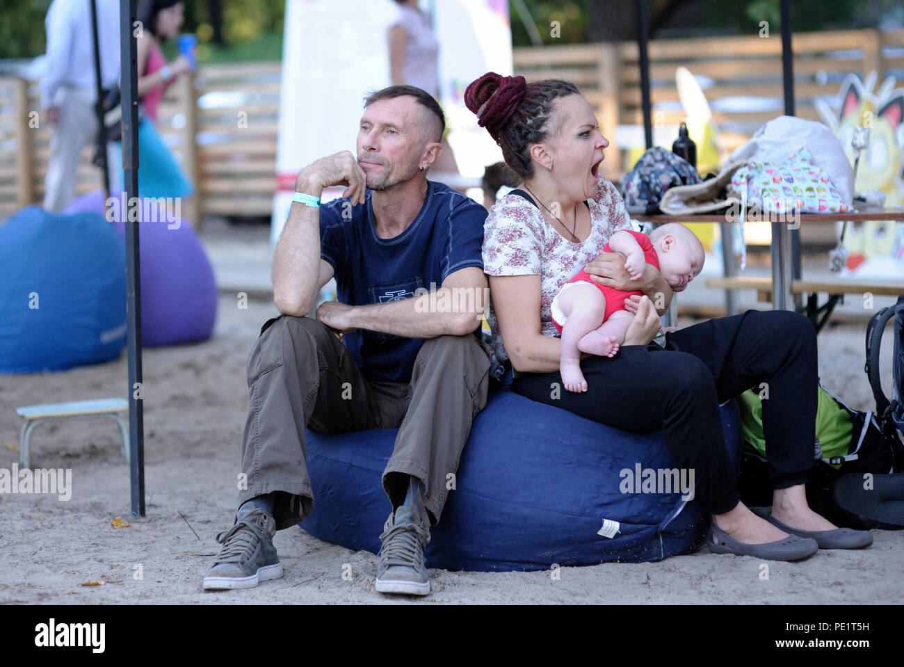 Un uomo e una donna con un bambino su mani in seduta bean bag, donna sbadigli. Fest di Yoga e cultura vedica "Vedalife-2018". Il 25 luglio 2018. A Kiev, Ucraina Foto Stock