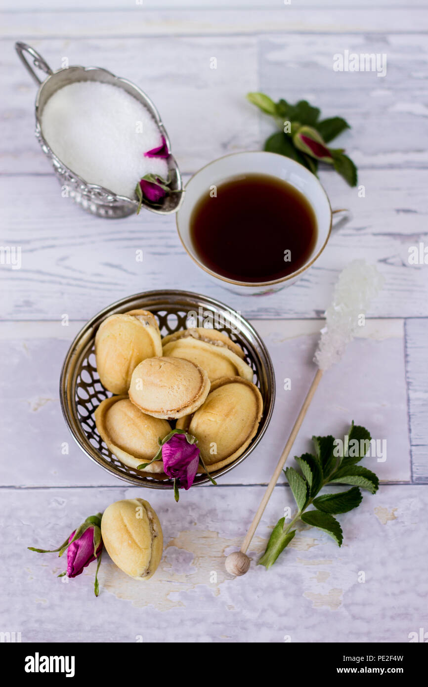 Tazza di tè, zucchero bianco, zucchero di canna, wild petali di rosa e biscotti fatti in casa chiamato dadi - piatto sullo sfondo dei laici Foto Stock