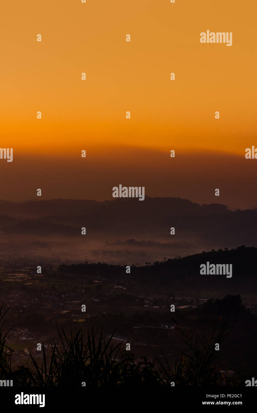 Vista del villaggio circondato da strati di nebbia e di montagna di albero in mattinata con cielo arancione Foto Stock