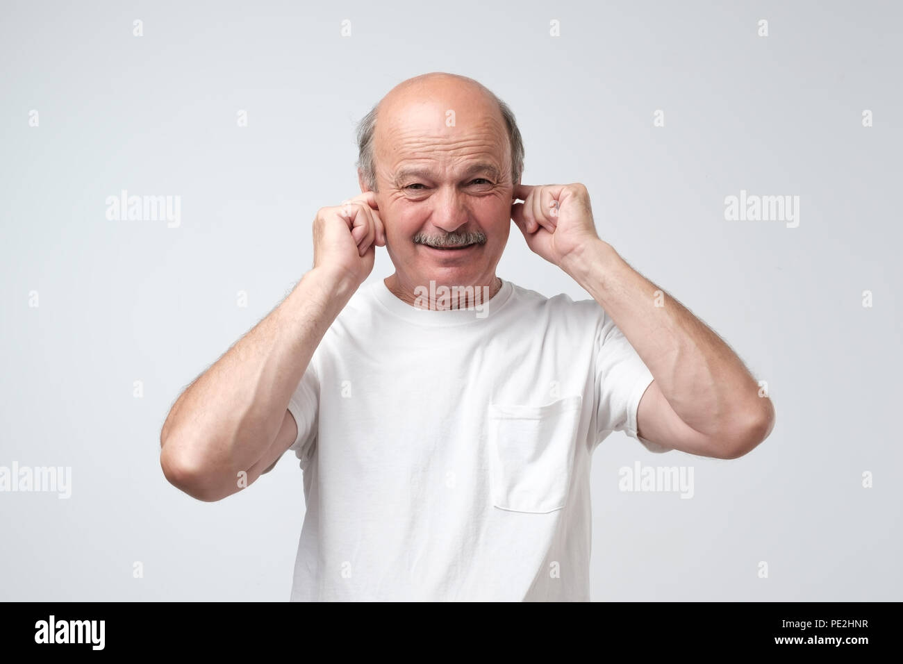 Stop che rumore forte concetto. Uomo maturo in bianco tshirt soffre di musica ad alto volume e di dolore cercando di collegare le orecchie contro uno sfondo grigio. Tristezza emoti Foto Stock Stop che rumore forte concetto. Uomo maturo in bianco tshirt soffre di musica ad alto volume e di dolore cercando di collegare le orecchie contro uno sfondo grigio. Tristezza emoti Foto Stock