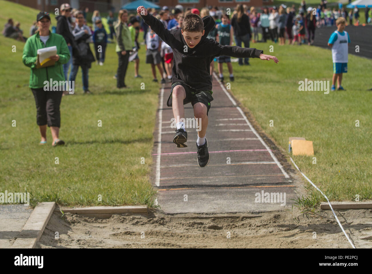 Giovane ragazzo in competizione in Track & Field del salto trple, indossa una felpa con cappuccio e pantaloni corti. Catturati a metà in aria. Modello rilasciato Foto Stock