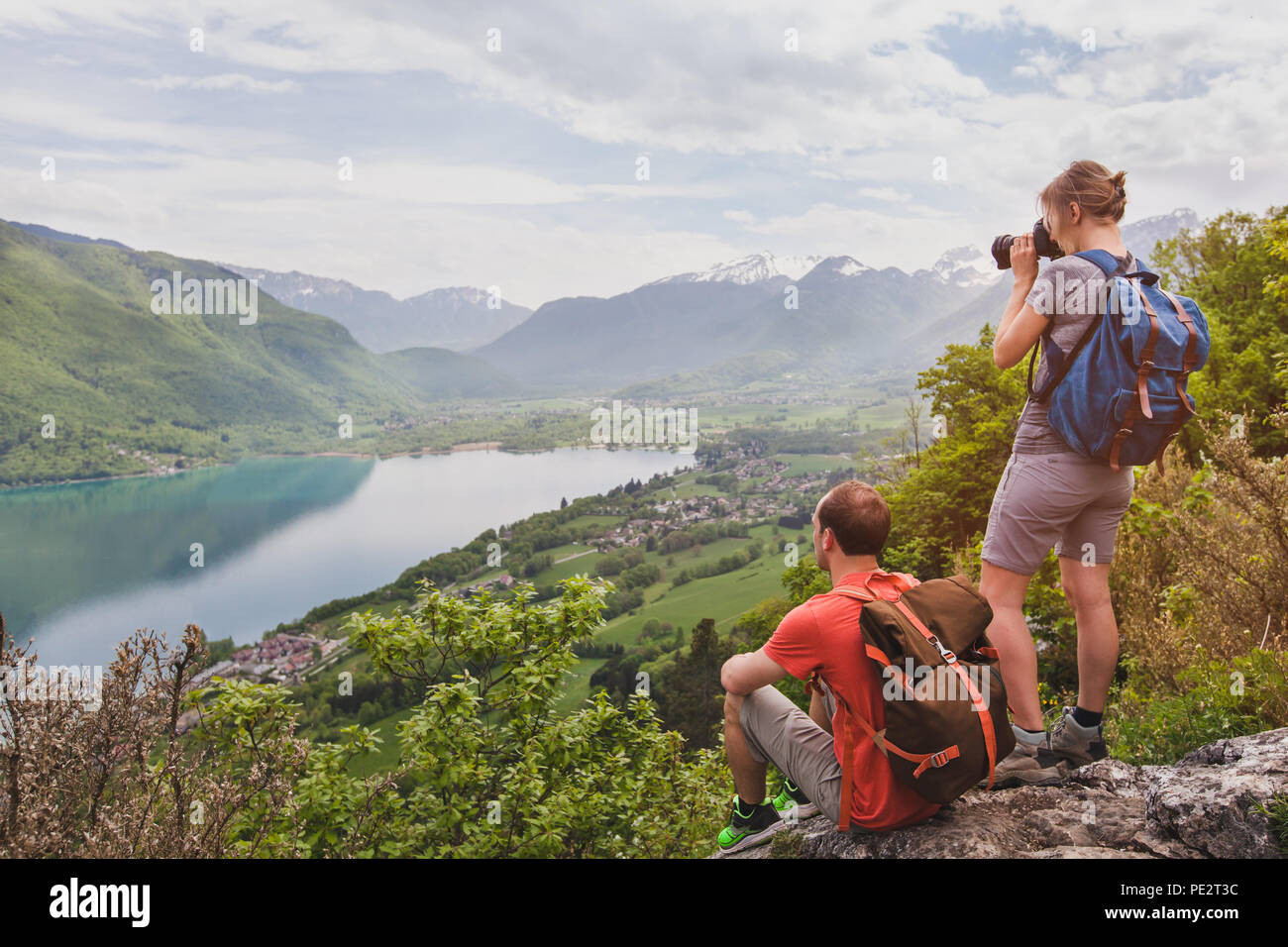 Viaggi e turismo, giovane coppia di viaggiatori con zaini godendo di una vista panoramica del lago, gli escursionisti rilassante sulla cima della montagna Foto Stock