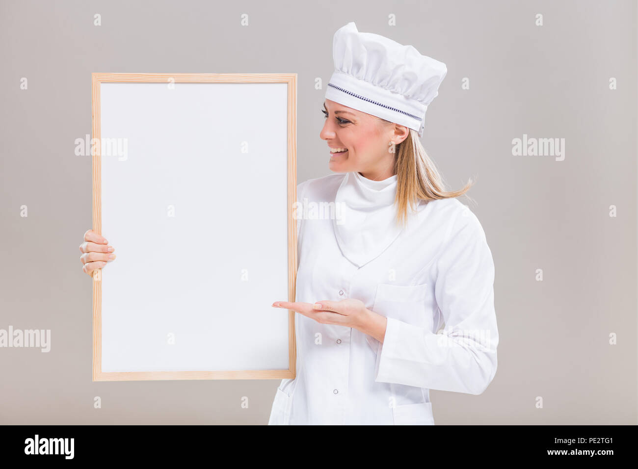 Ritratto di belle donne chef che mostra la lavagna vuota su sfondo grigio. Foto Stock