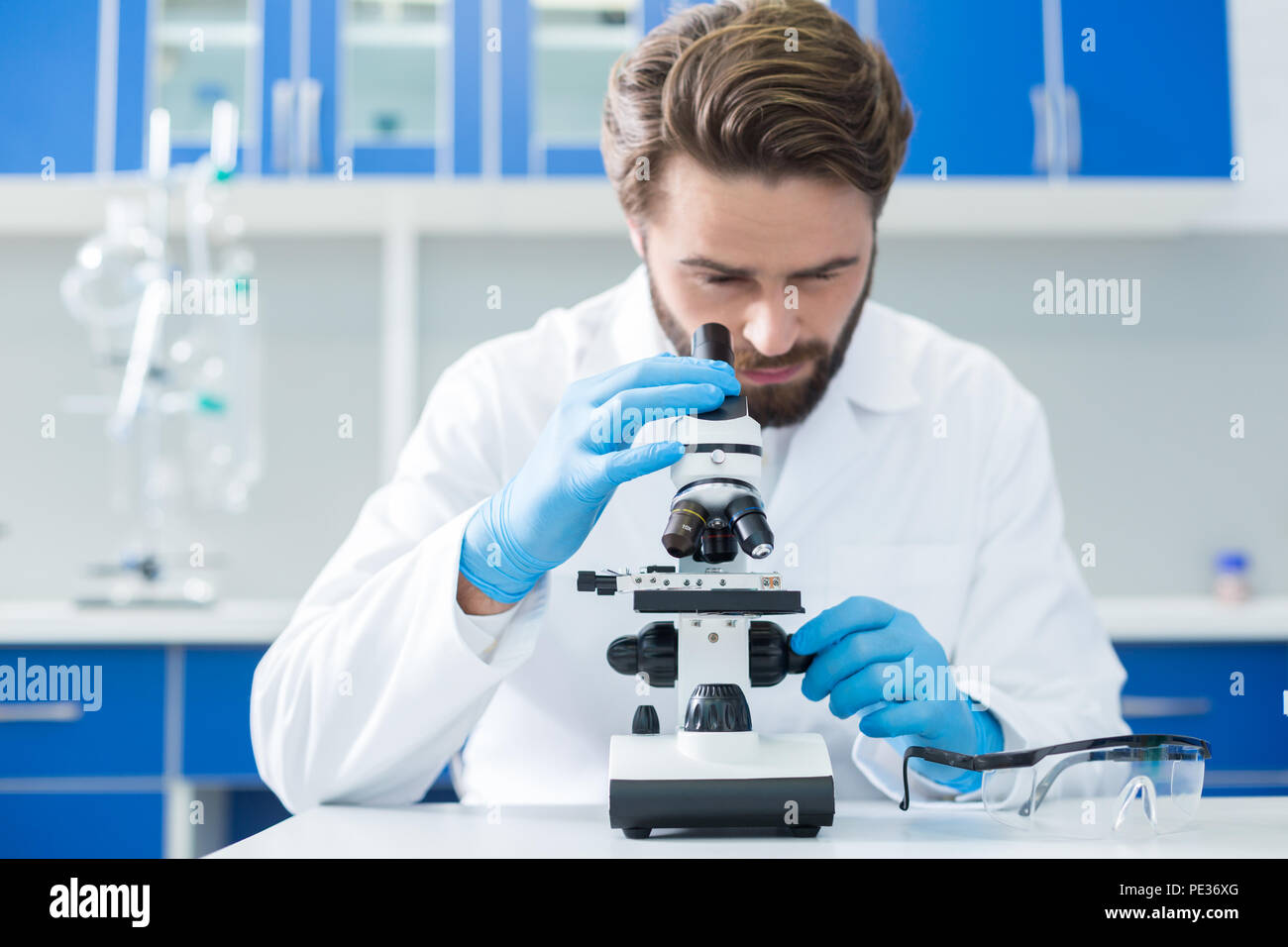 Attrezzature tecniche. Messa a fuoco selettiva di un moderno microscopio in piedi sulla tavola mentre viene utilizzato da un bel bello scienziato professionale Foto Stock