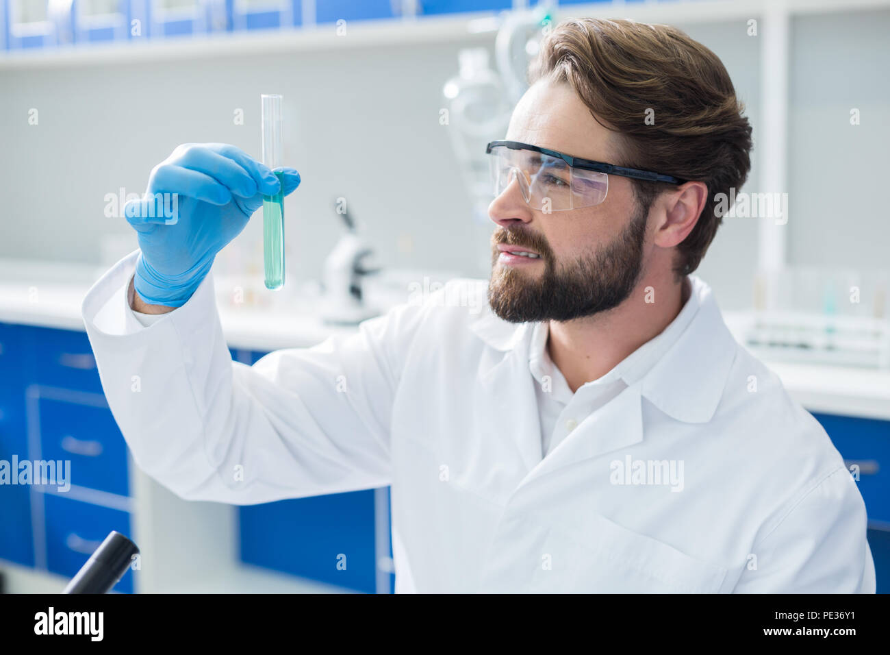 Esperimento di chimica. Nice positivo uomo gravi indossando occhiali protettivi e trattenere un tubo di prova durante un esperimento chimico Foto Stock