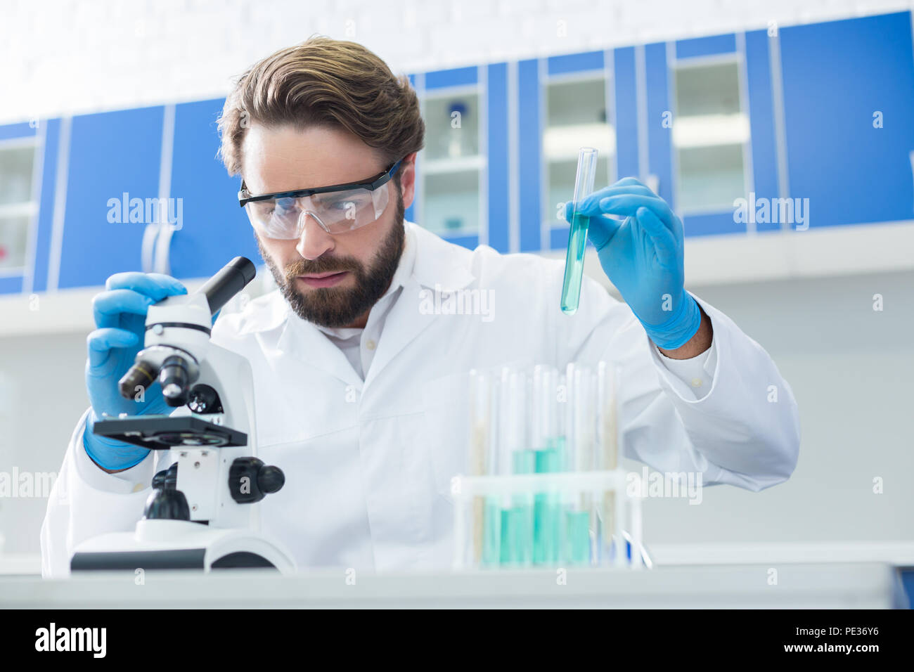 La scienza moderna. Grave piacevole intelligente uomo seduto al tavolo e trattenere un tubo di prova durante il lavoro in laboratorio Foto Stock