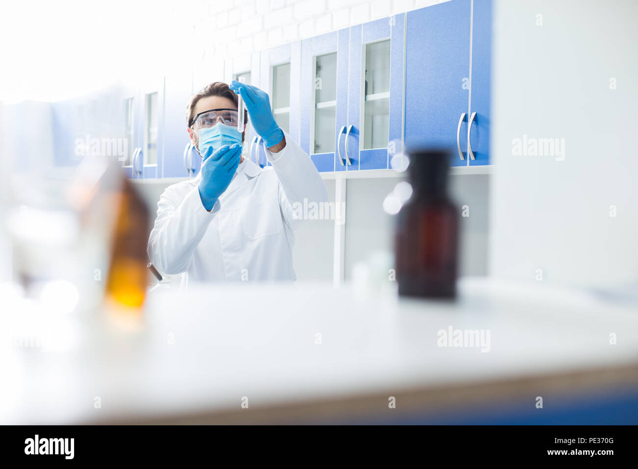 Ingegneria biologica. Smart maschio professionale biologo tenendo una provetta e indossare una maschera mentre si conduce una ricerca in laboratorio Foto Stock