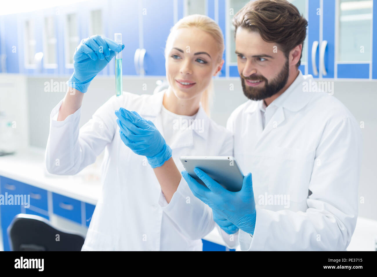 La cooperazione degli scienziati. Smart piacevole bella donna in piedi vicino al suo collega e guardando la provetta mentre studiano insieme con lui Foto Stock