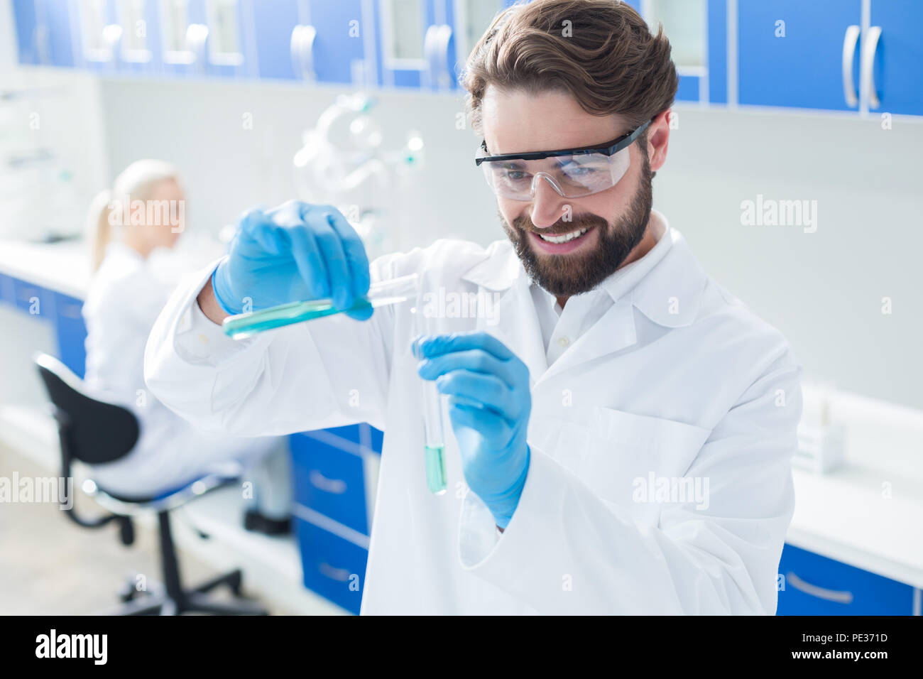 Scienziato entusiasta. Positivo felice lieto uomo che indossa gli occhiali di protezione e sorridenti mentre si lavora con reagenti chimici Foto Stock