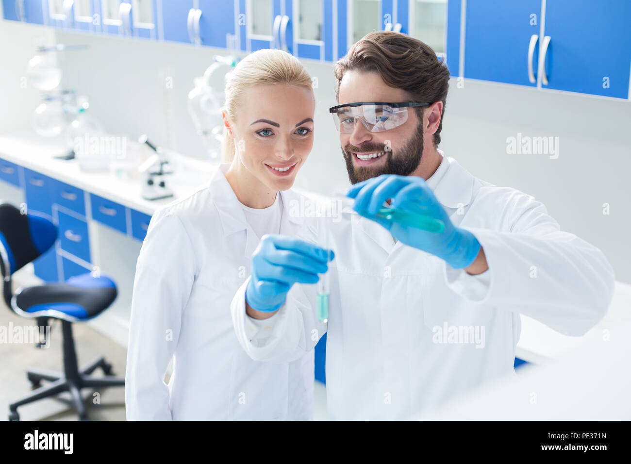 Esperimento di successo. Nice positivo scienziato felice guardando le provette e sorridente durante la conduzione di un esperimento di successo Foto Stock