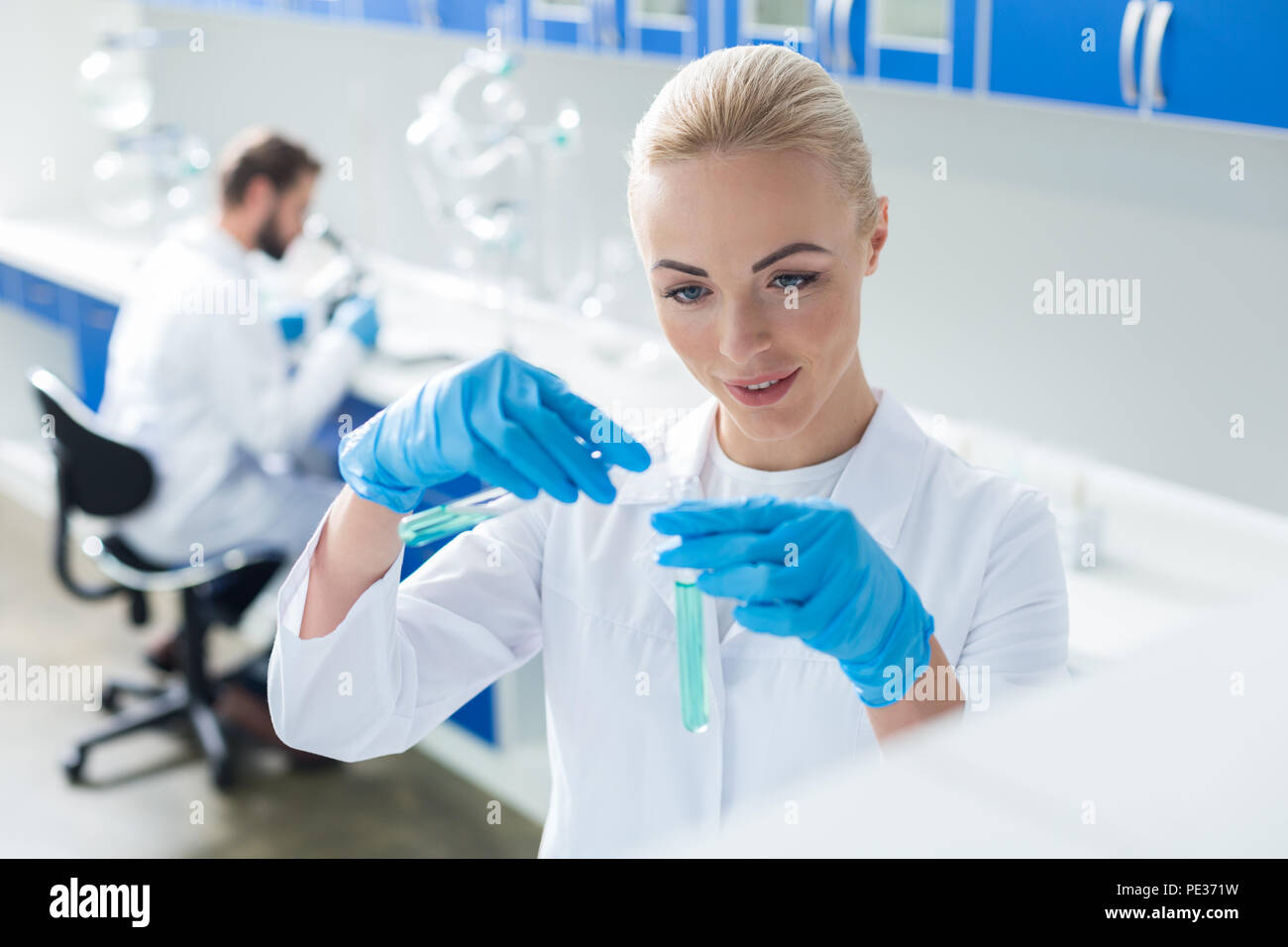 Analisi chimica. Bella Allegra donna bionda azienda provette e facendo analisi chimica del liquido durante il lavoro in laboratorio Foto Stock