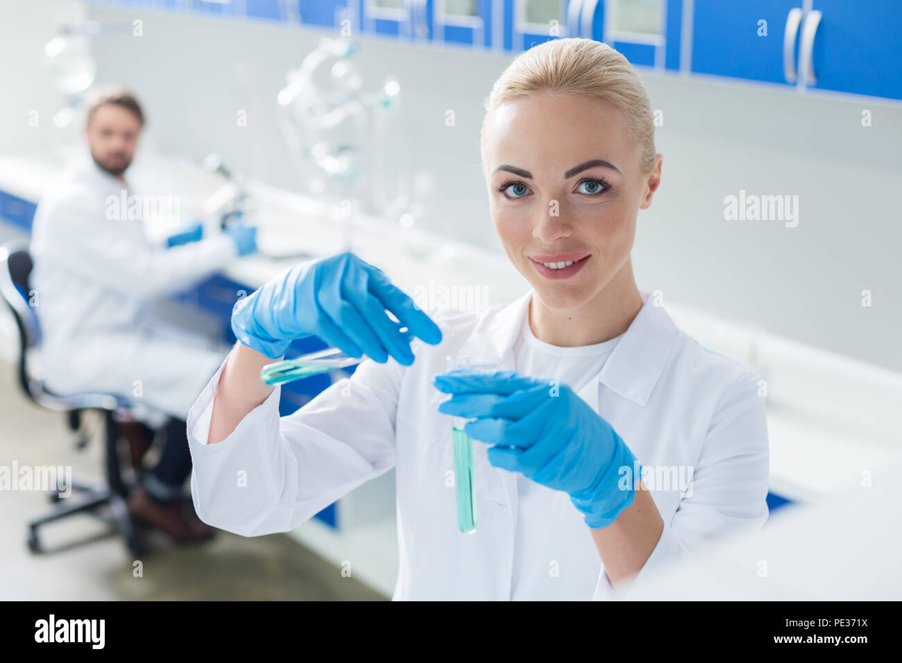 Il chimico esperto. Felice smart positivo donna sorridente e guardando a voi mentre si lavora con campioni chimici Foto Stock