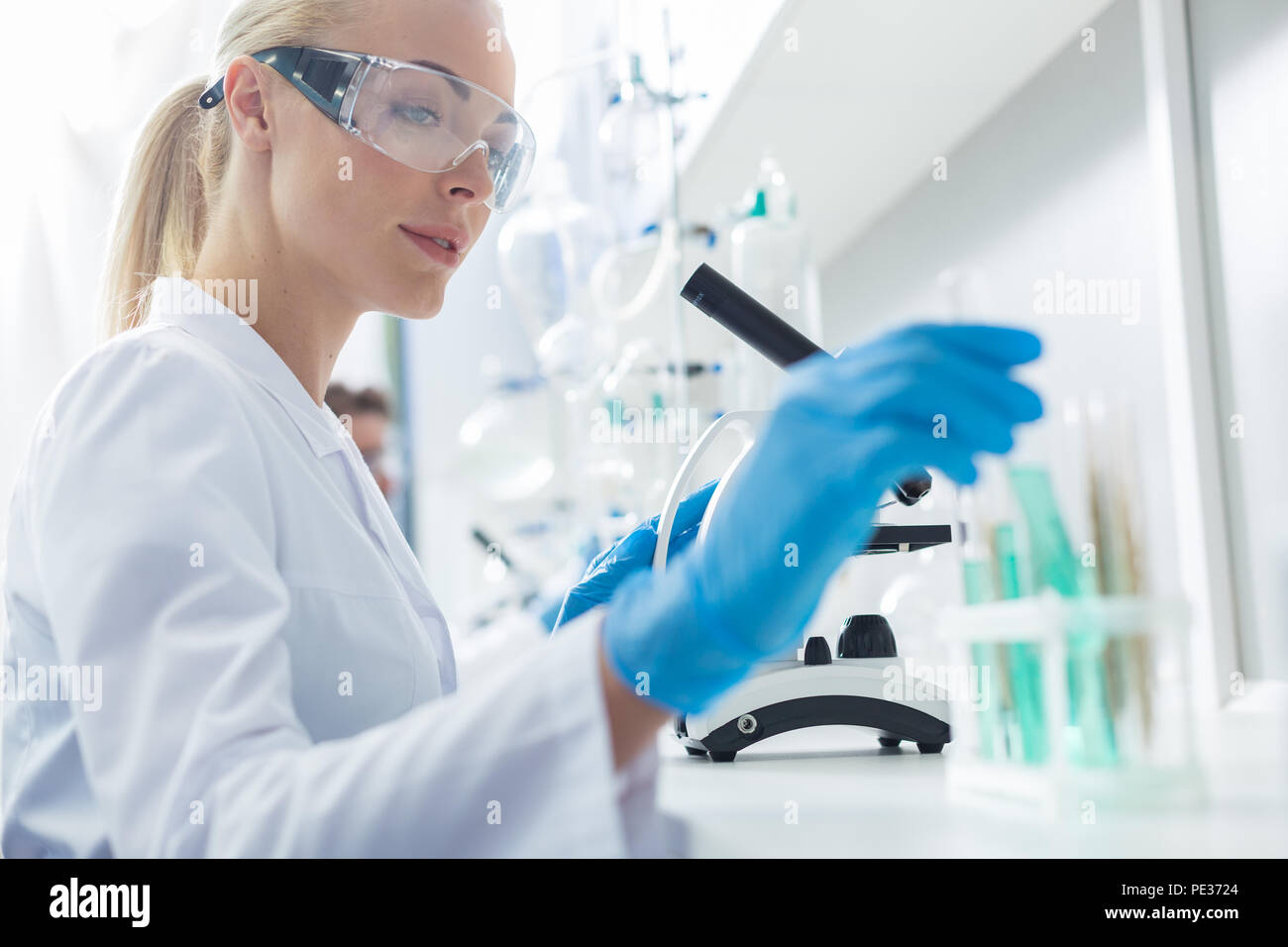 Reagenti pericolosi. Nizza smart positivo donna che indossa gli occhiali di protezione e lavorare con reagenti pericolosi mentre si esegue una ricerca in campo chimico la Foto Stock