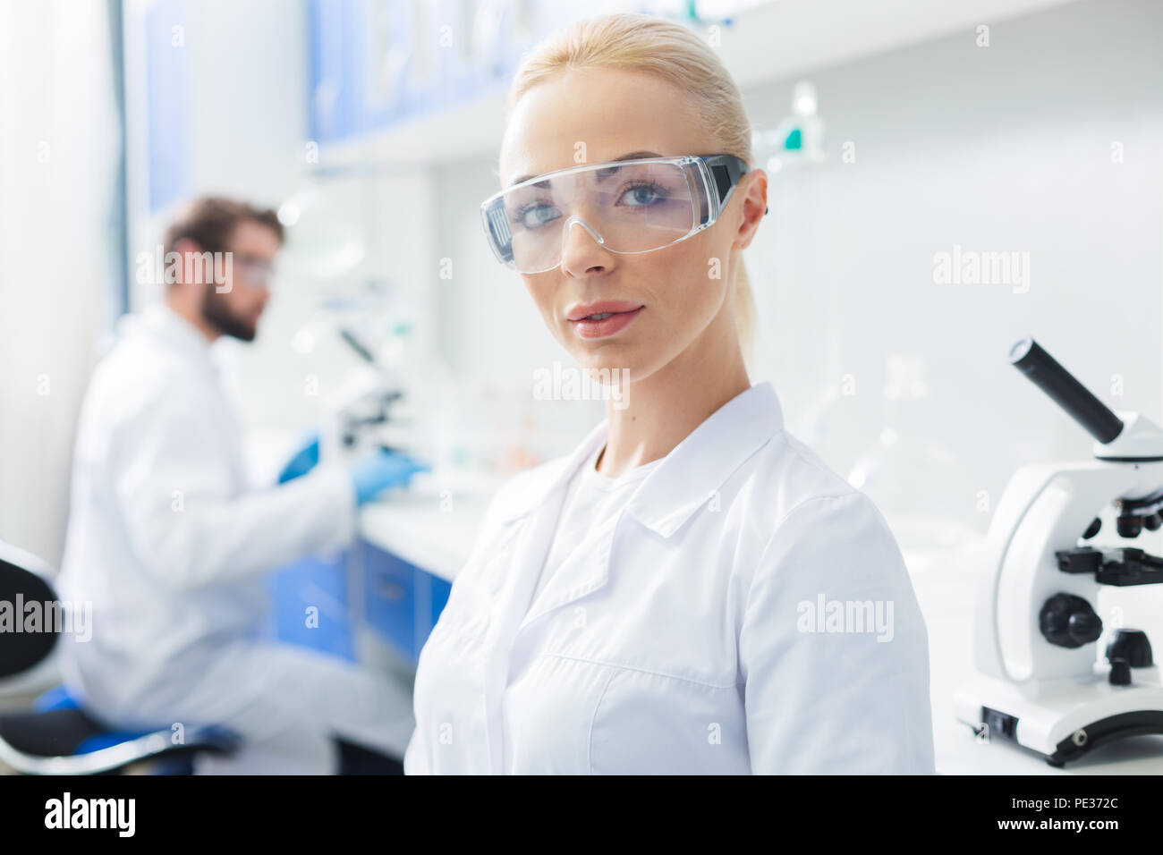 La scienza lavoratore. Ritratto di una allegra donna scienziato indossando occhiali protettivi e guardando a voi durante il lavoro in laboratorio Foto Stock