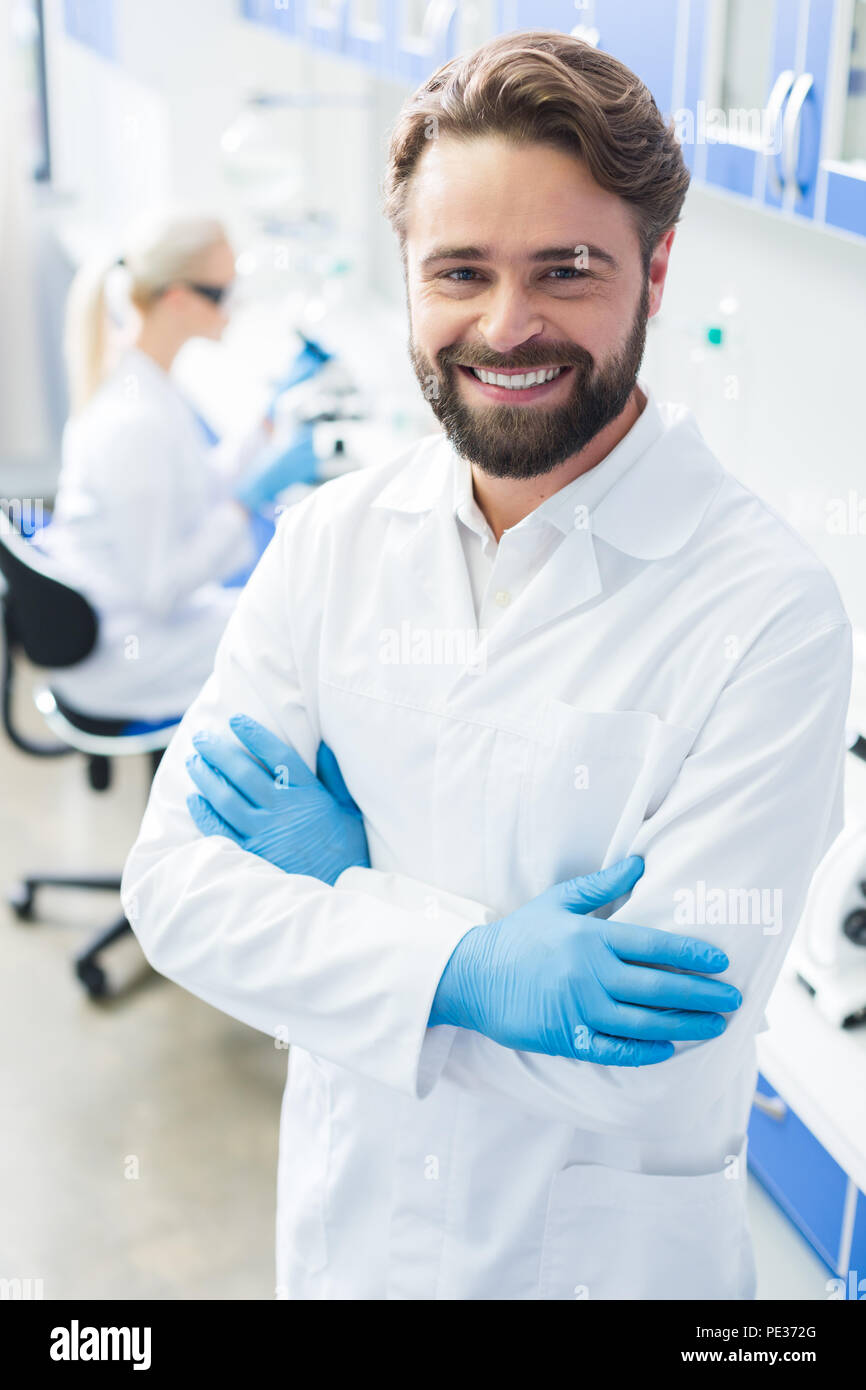 Ricercatore professionista. Piacevole bello bello farmacia in piedi in laboratorio e guardando a voi mentre sono in un buon umore Foto Stock