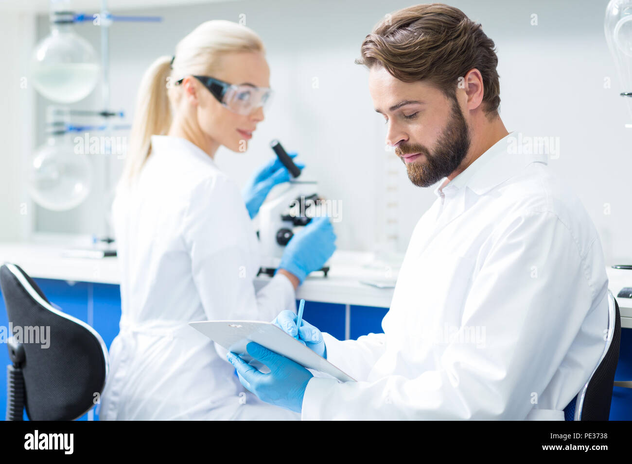 Osservazioni professionali. Smart gravi scienziato barbuto seduto in laboratorio e prendere appunti mentre scrivere le sue osservazioni Foto Stock
