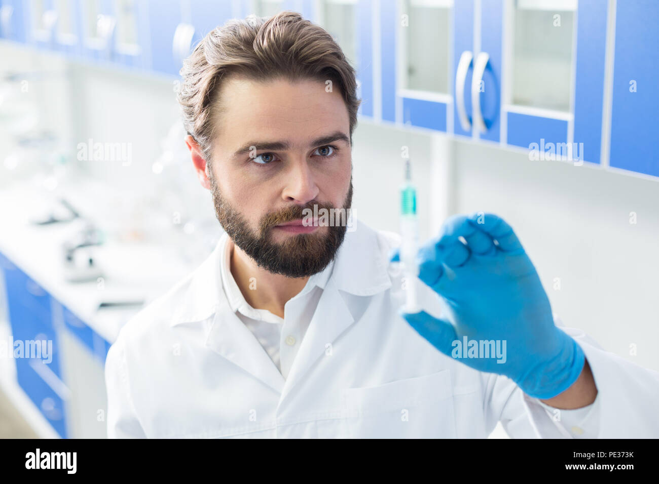 Laboratorio ospedaliero. Smart nizza scienziato maschio di foratura di una siringa e lo sta guardando mentre si lavora nel laboratorio ospedaliero Foto Stock