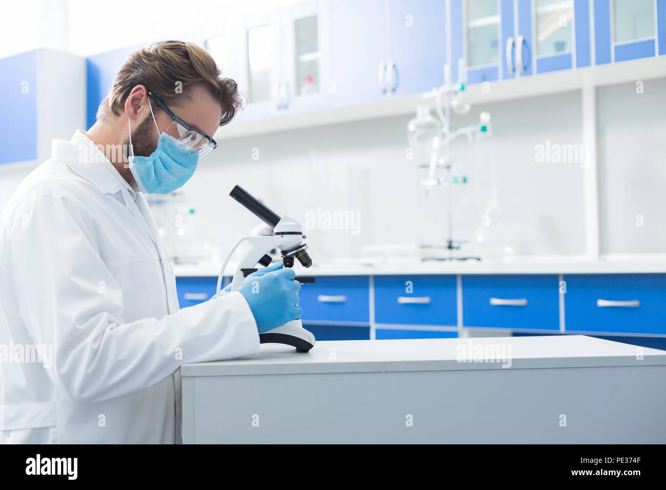 Professional biologo. Smart bell uomo bello in piedi vicino al microscopio e cercando in esso mentre si lavora come un biologo in laboratorio Foto Stock