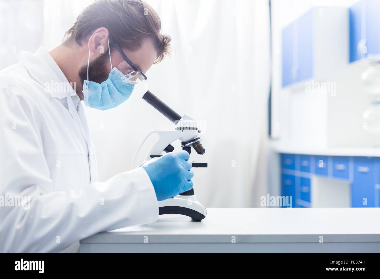 Lavoro interessante. Grave intelligente di Nizza uomo seduto in laboratorio e cercando nel microscopio mentre lavora come un biologo Foto Stock