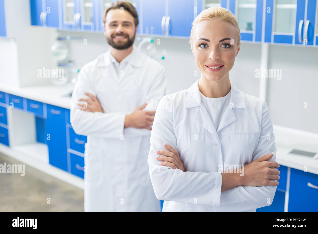 Ricercatore femmina. Felice bella donna bionda cross permanente consegnato e guardando a voi mentre in piedi in laboratorio Foto Stock