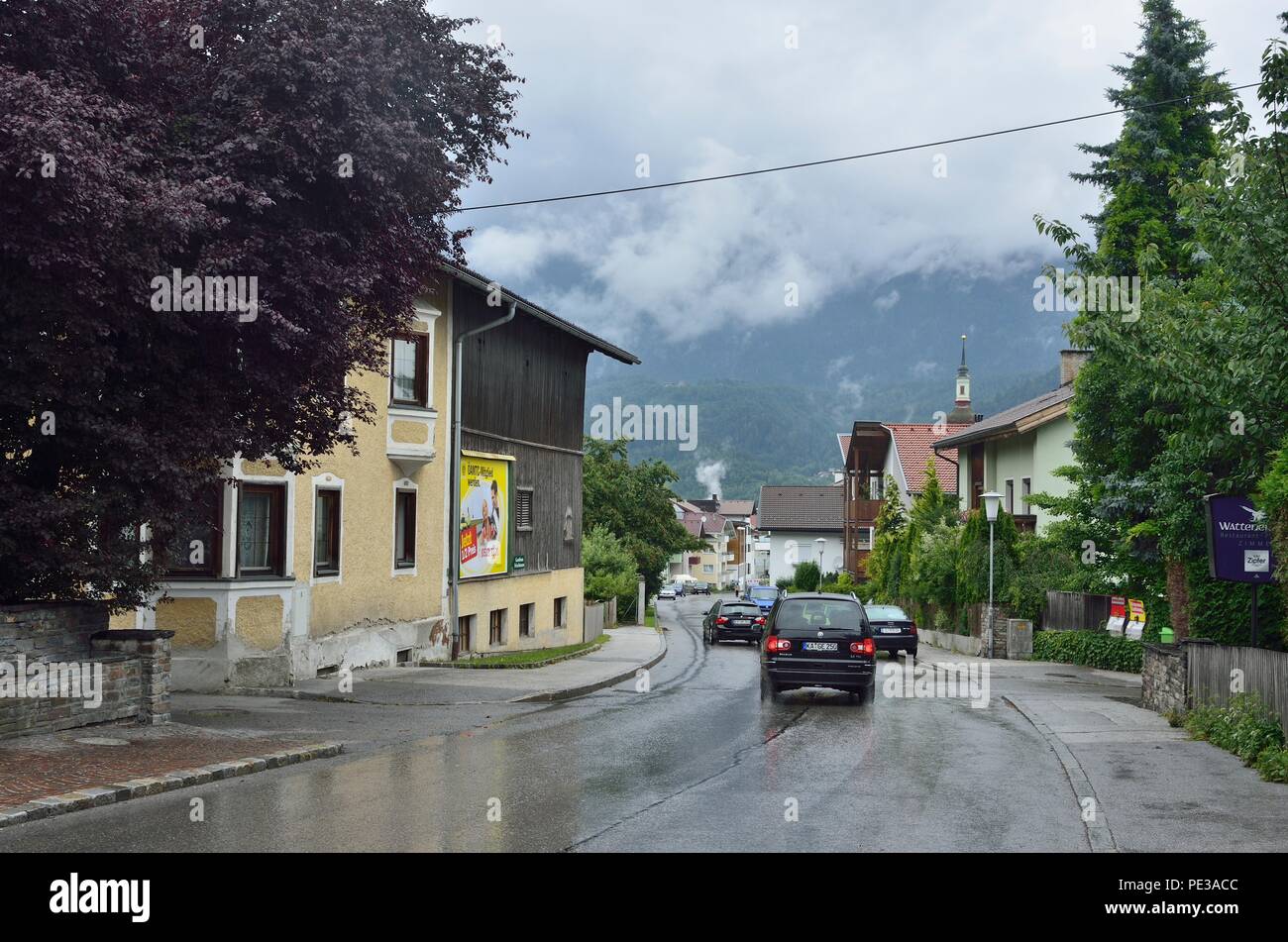 Una scena tipica di case su entrambi i lati di una strada stretta con le automobili che si plying sopra. Alpi catene montuose sullo sfondo, Wattens, Austria, Europa Foto Stock