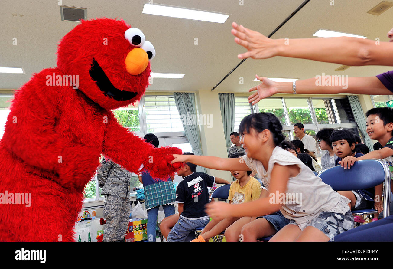 Elmo di Sesame Street carattere, scuote la mano con i bambini da un orfanotrofio in città Itoman sett. 22, 2015, Okinawa, in Giappone. Stati Uniti Air Force Senior Airman Alexander marrone da xviii Communications Squadron, indossa un Elmo di Sesame Street carattere, per intrattenere e interagire con i bambini durante il XVIII CS visita a donare presenta per i bambini che erano nel bisogno. (U.S. Air Force foto di Naoto Anazawa) Foto Stock