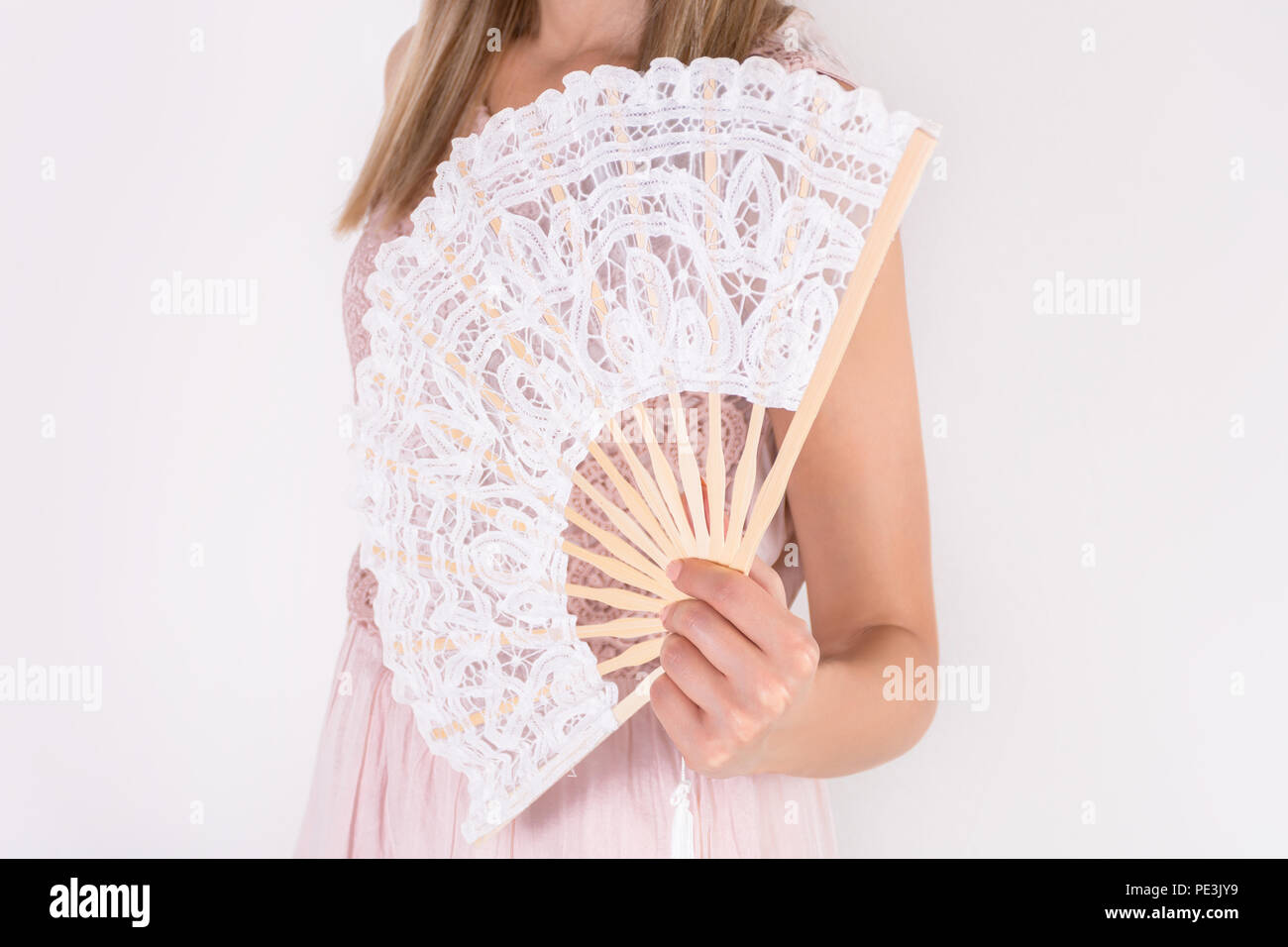 Bella giovane femmina in crema di azienda Abito in pizzo bianco Ventilatore a mano isolati su sfondo bianco. Estate e concetto di calore. Close up, il fuoco selettivo Foto Stock