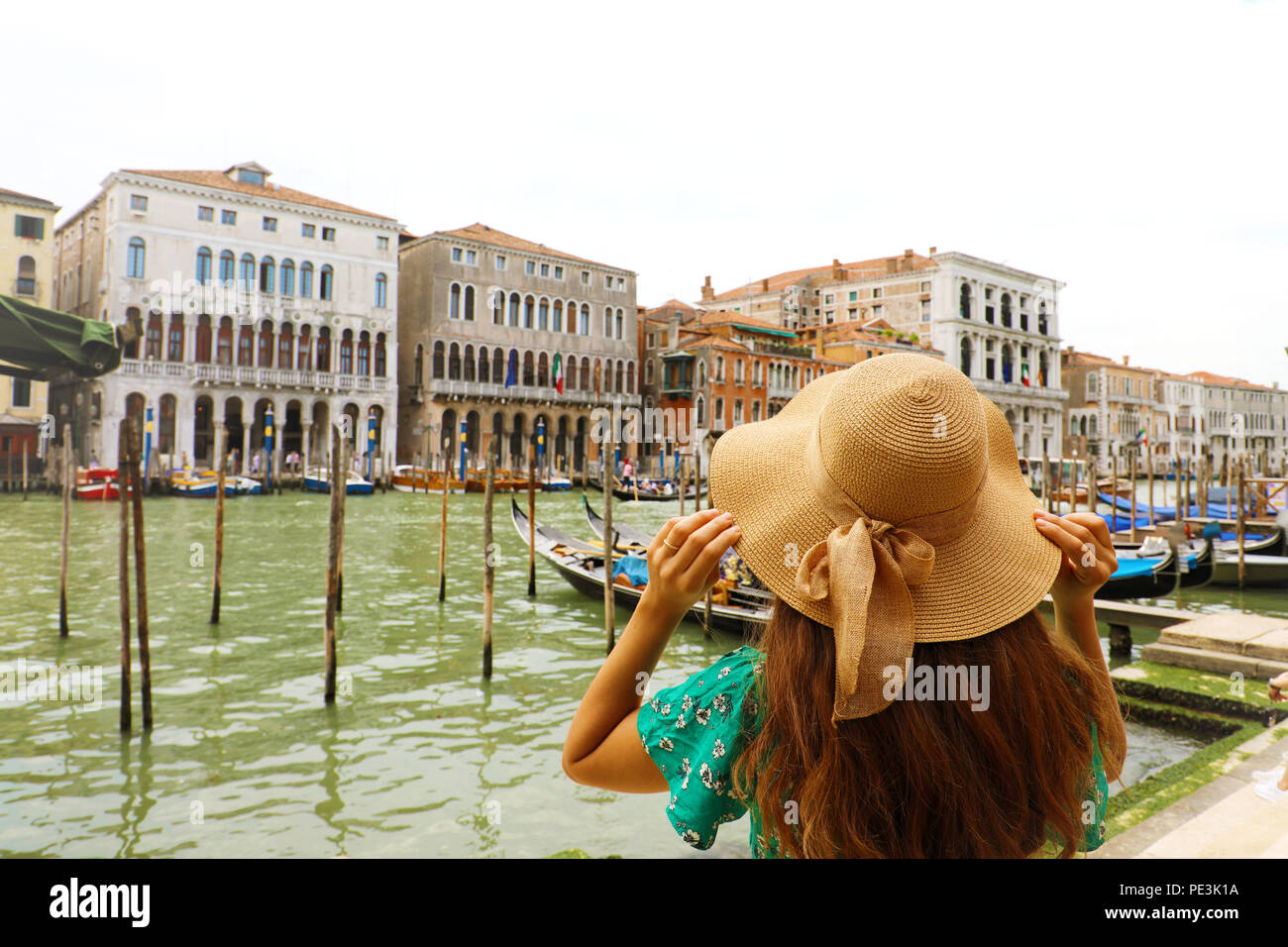 Giovane donna con abito verde mentre tiene il suo cappello quando cercando di Venezia Canal Grande. Vista posteriore della ragazza di viaggiatori a Venezia, Italia. Foto Stock