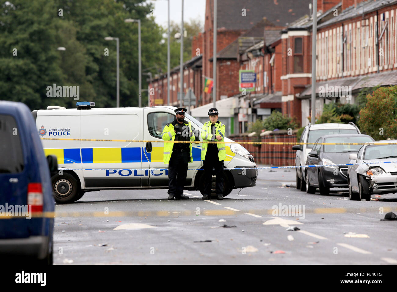 Gli ufficiali di polizia stand presso il cordoned fuori area in Claremont Road, Moss Side, Manchester, dove molte persone sono state ferite dopo una ripresa. Foto Stock