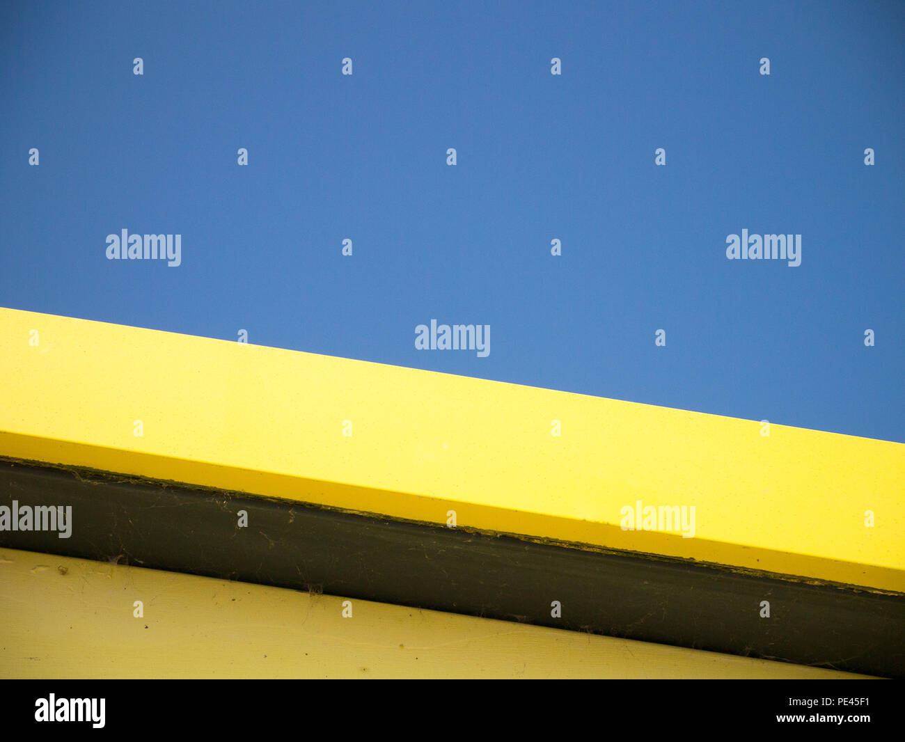 Colore fino in prossimità del bordo del tetto giallo di un beach hut, colpo dal basso contro un cielo blu chiaro Foto Stock