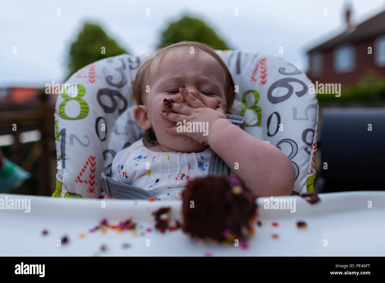 Un bambino di mangiare la sua torta di compleanno per la sua sedia alta Foto Stock