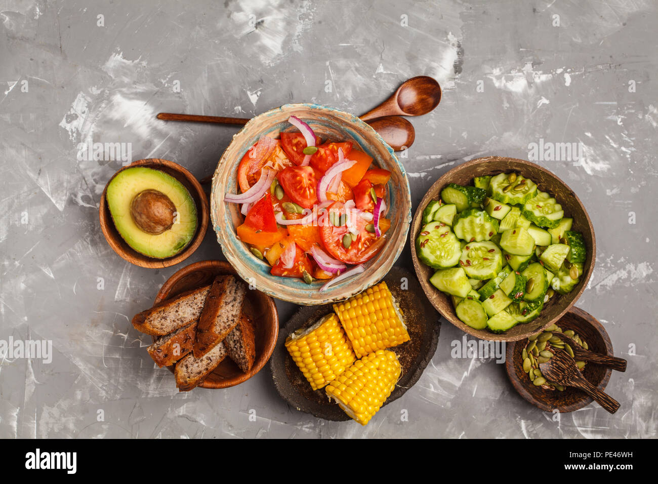 Pulire il concetto di mangiare. Insalata di cetrioli, insalata di pomodoro, pane di lino, avocado, mais. Vista superiore, cibo sfondo. Foto Stock