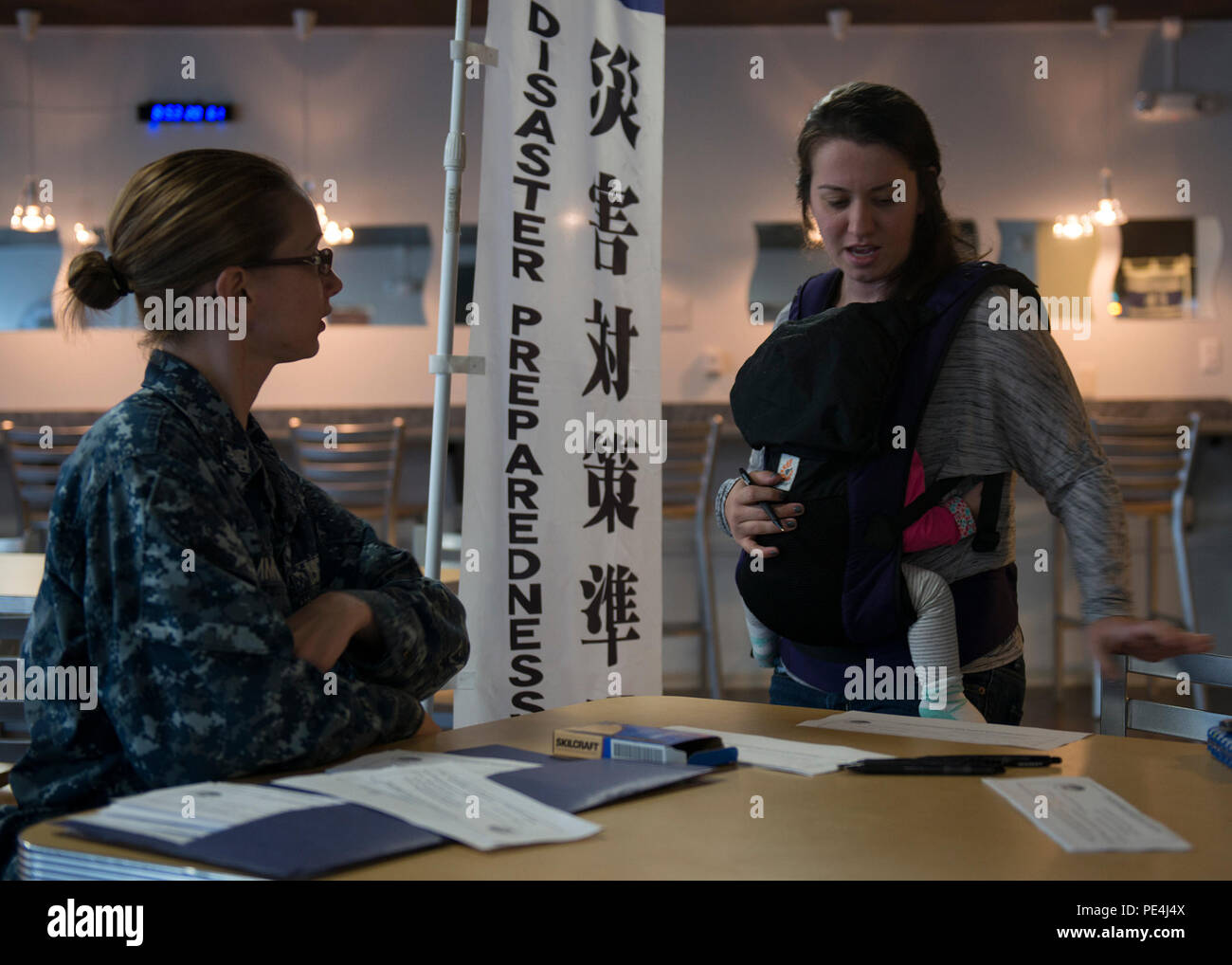 Un rappresentante della gestione delle emergenze della Marina degli Stati Uniti assiste un membro della comunità di base con l'iscrizione al computer Desktop Notification System presso la Naval Air Facility Atsugi, Giappone, il 17 settembre 2015. L'immagine mostra una tabella di informazioni impostata in un'area pranzo comune in cui il personale può registrarsi per ricevere avvisi e-mail automatici. Il sistema è progettato per notificare rapidamente ai membri della comunità militare e civile emergenze, pericoli meteorologici e incidenti in tutta la base per migliorare la sicurezza e la preparazione. Foto Stock