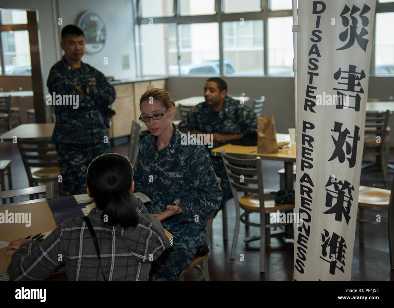 Un rappresentante della gestione delle emergenze della Marina degli Stati Uniti assiste i membri della comunità Atsugi della Naval Air Facility con l'iscrizione al computer Desktop Notification System in un bar di base in Giappone il 17 settembre 2015. L'immagine raffigura una tabella di informazioni con personale utilizzato per promuovere la registrazione per gli avvisi e-mail automatici. Il sistema migliora la preparazione alle emergenze garantendo una rapida diffusione delle informazioni ufficiali in caso di calamità naturali, incidenti di sicurezza e emergenze di installazione. Foto Stock