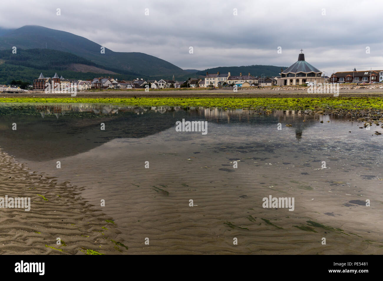 Vista dalla spiaggia con la bassa marea con edifici tra cui la Chiesa riflessa nell'acqua. Newcastle ai piedi della Mourne Mountains in N.Irlanda. Foto Stock