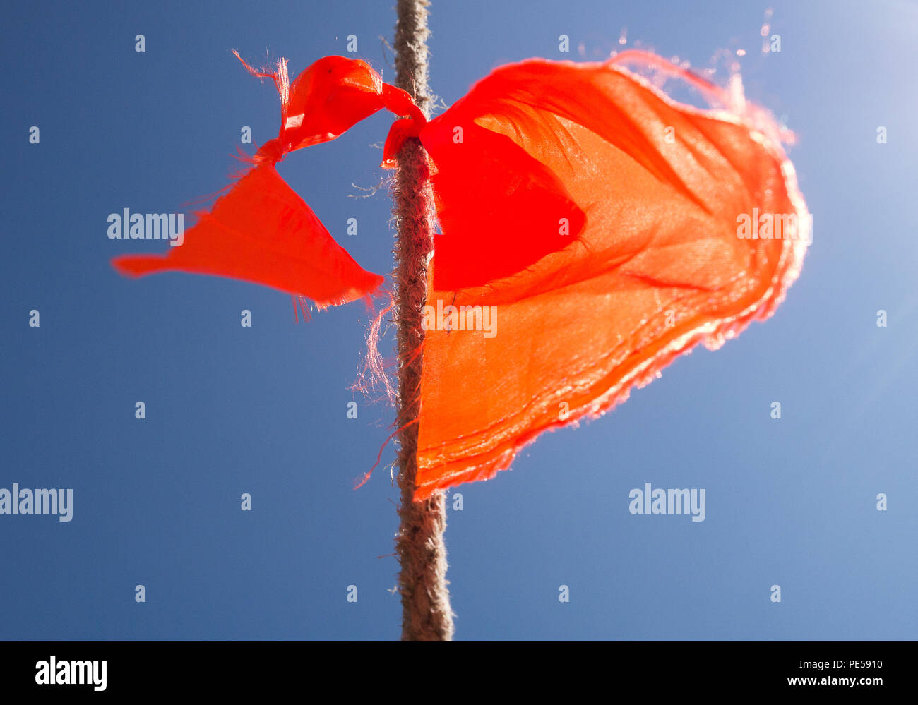 Immagine a colori di un arancione sfilacciata bunting bandiera su una fune, colpo dal basso contro un cielo blu chiaro Foto Stock