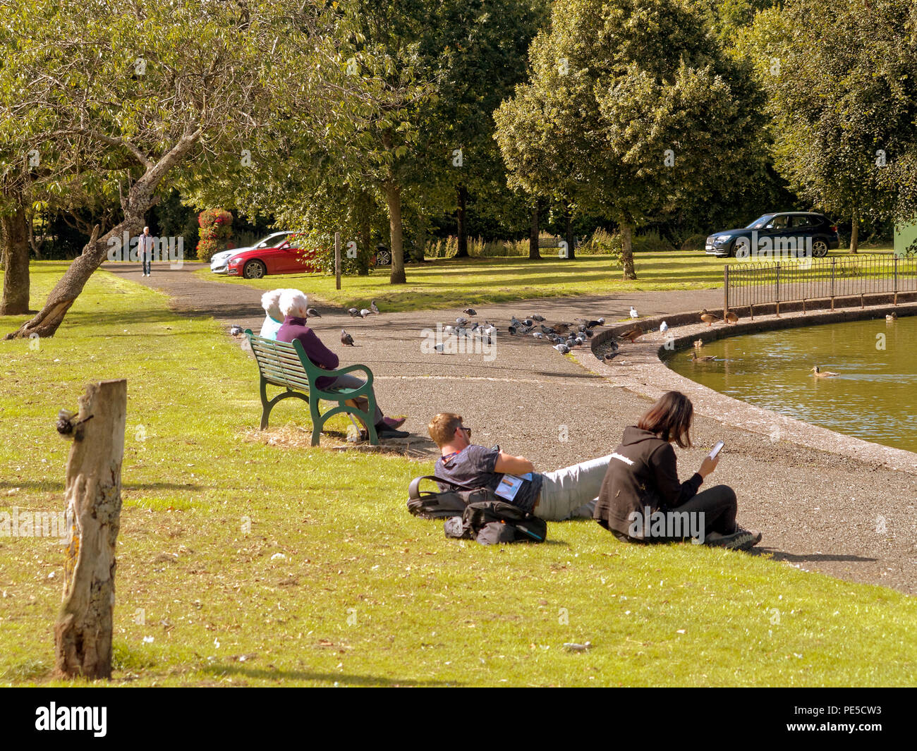 Parco Knightswood pond park life soleggiata giornata estiva gente seduta gode di clima caldo Foto Stock