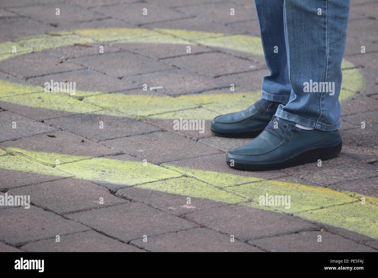Una persona in piedi sul nastro giallo pattern strada 'arte' dipinta sul sentiero a Canberra CBD e principale area turistica. Foto Stock