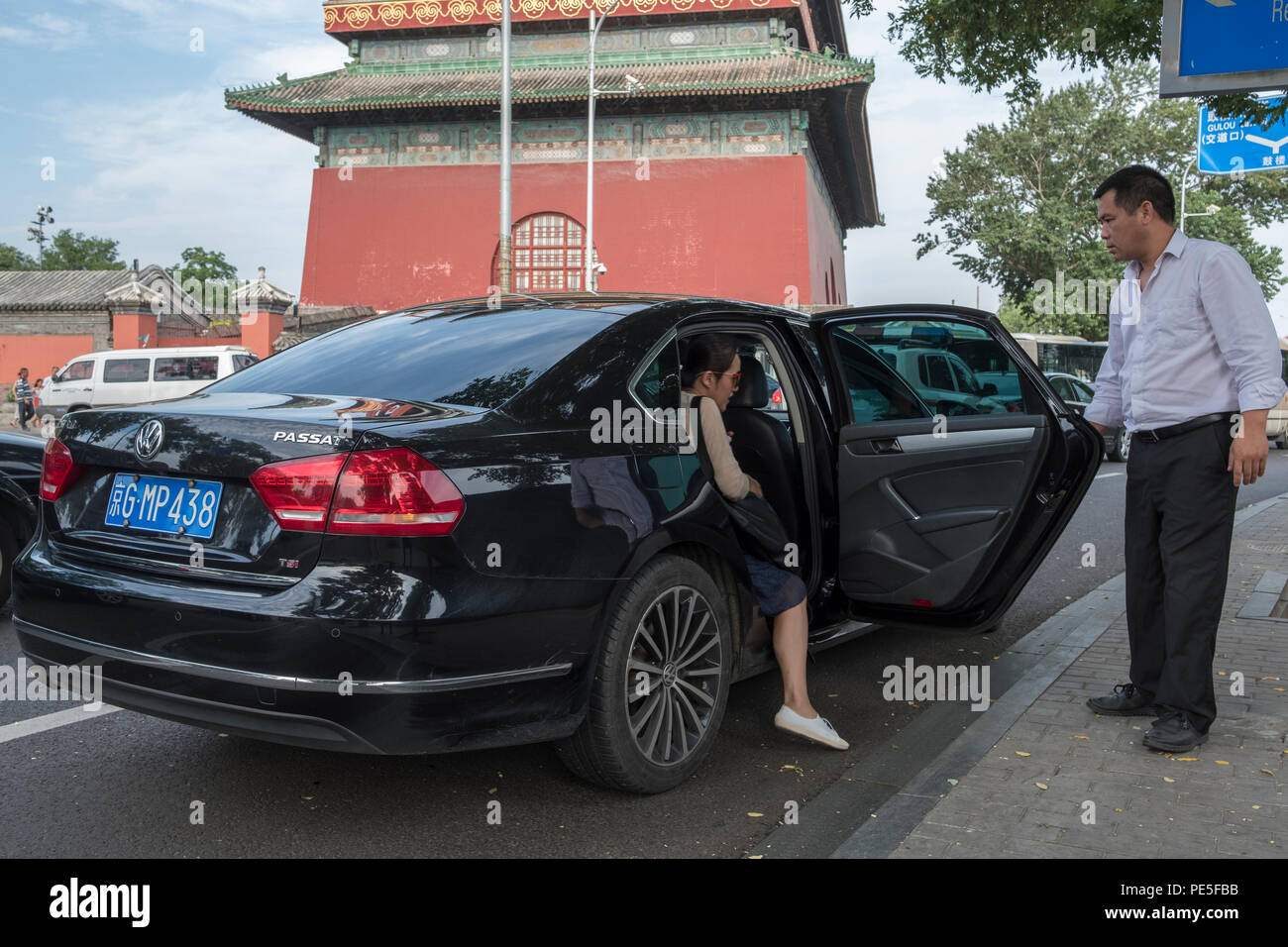 Una donna cinese che entra in una macchina Didi Premier assistita dal pilota Zhao di fronte alla tradizionale Torre del tamburo nel centro di Pechino, in Cina. Didi premi Foto Stock