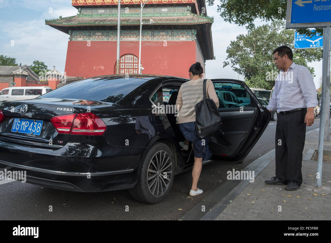 Una donna cinese che entra in una macchina Didi Premier assistita dal pilota Zhao di fronte alla tradizionale Torre del tamburo nel centro di Pechino, in Cina. Didi premi Foto Stock