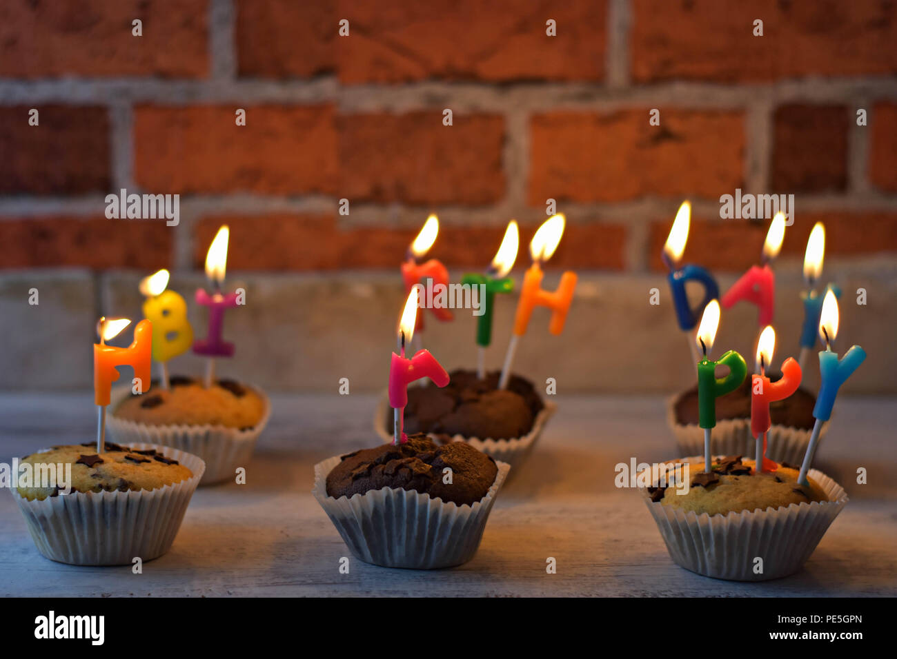 Deliziosi muffin-tortini di masterizzazione di pentecoste buon compleanno candele ad un muro di mattoni come sfondo/ Happy Birthday Celebration scheda/ biglietto di auguri Foto Stock