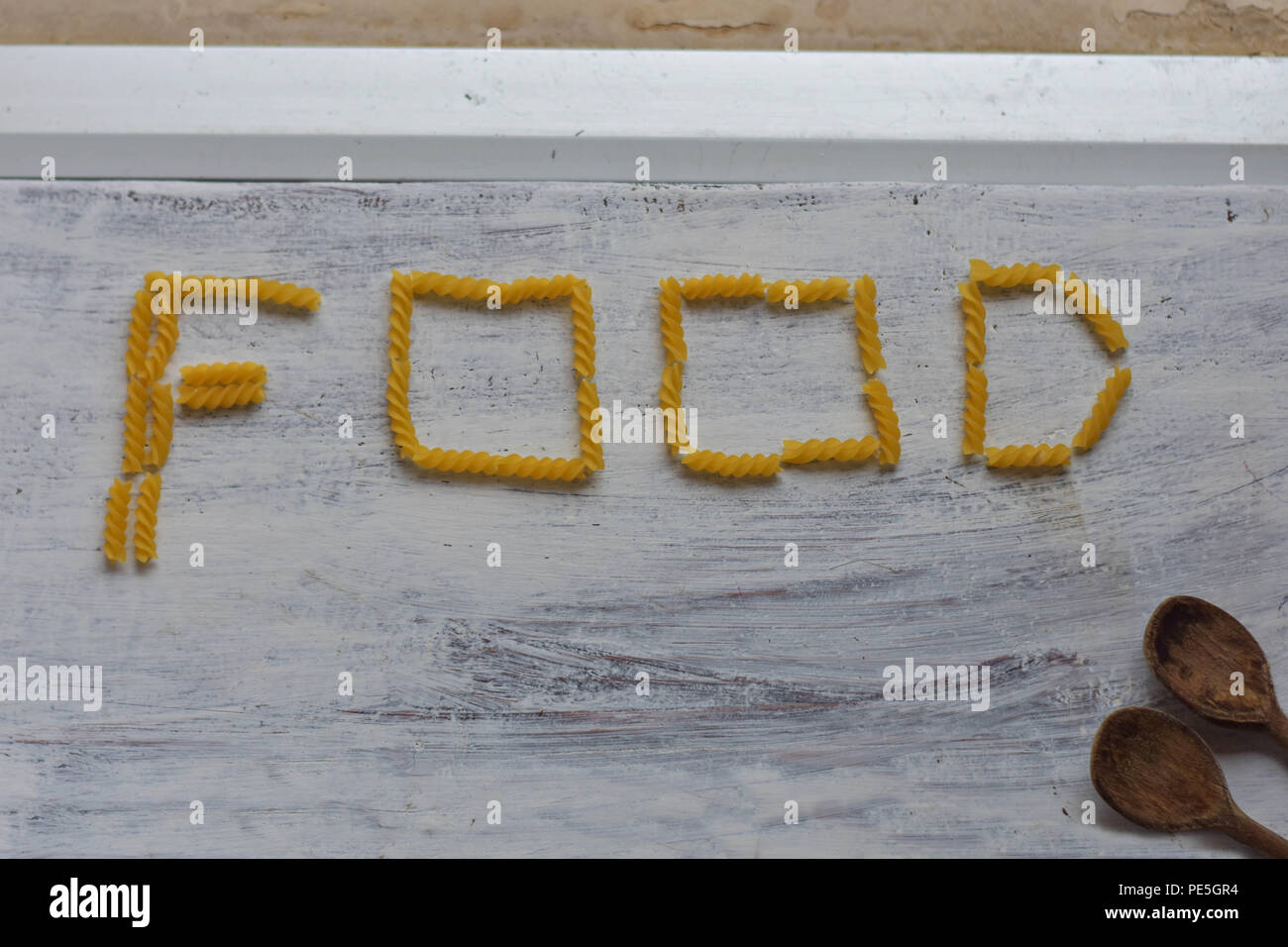 Iscrizione "alimentare" whit maccheroni e due cucchiai di legno alla luce in legno bianco come sfondo immagine concettuale del cibo-cucina sullo sfondo Foto Stock
