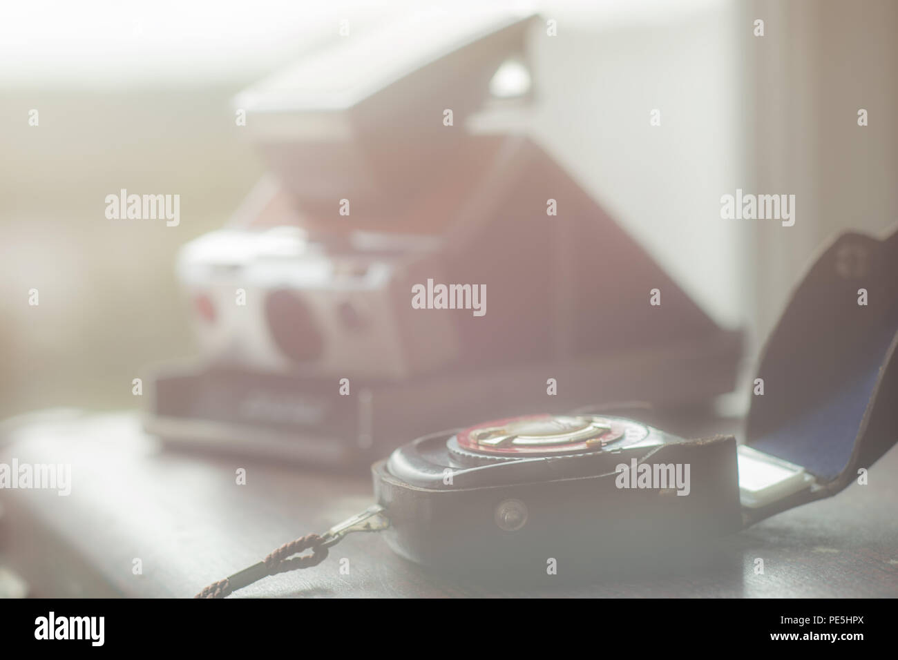 Un vintage Istantanea telecamera e un esposimetro giacciono sulla superficie di una vecchia valigia in una bella luce Foto Stock