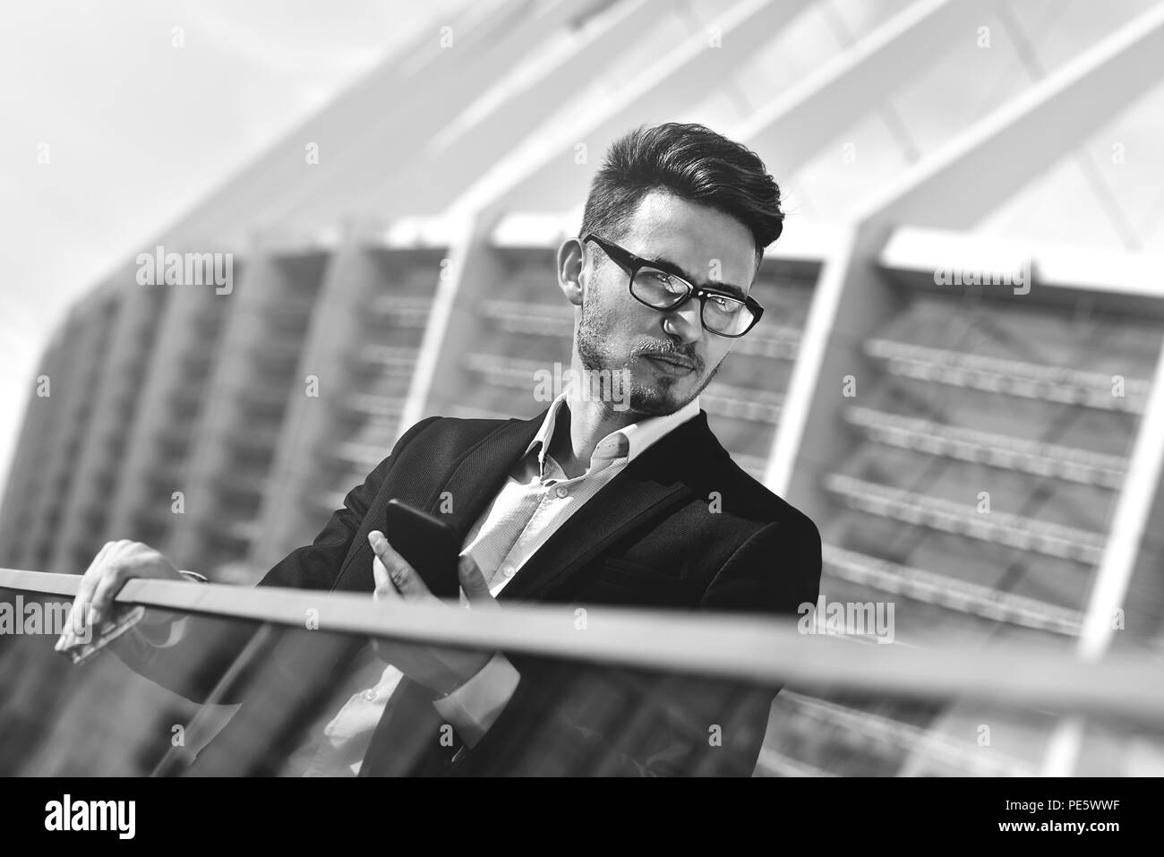 Imprenditore moderno. Fiducioso giovane uomo in tuta completa in piedi all'aperto con panorama urbano in background utilizzando uno smartphone Foto Stock