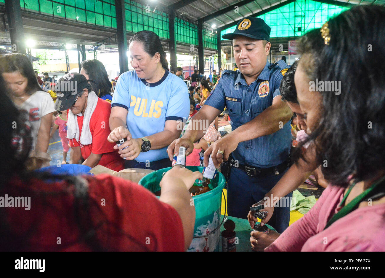 Quezon City, Filippine. 13 Ago, 2018. I volontari insieme al funzionario di polizia (PO3) Casinao (terza da sinistra) e funzionario di polizia (PO1) Hunrubia della stazione di polizia 6 sono impegnati per la preparazione del cibo per essere distribuito agli sfollati che sono stati vittime delle piogge monsoniche in Barangay Bagong Silangan, Quezon city, Filippine. Credito: Robert Oswald Alfiler/Alamy Live News. Foto Stock