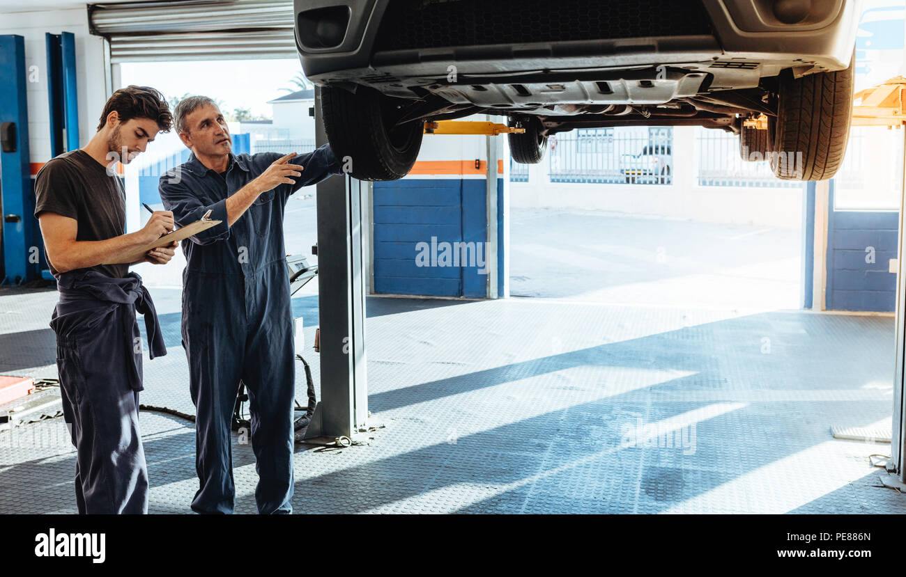 Due meccanici in uniforme di esaminare la vettura e di rendere note per le riparazioni da fare. Mechanic rendendo elenco dei malfunzionamenti di auto. Foto Stock